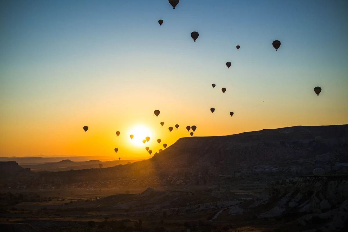 Hot-air balloons rising into a golden sunrise above the valleys of Cappadocia